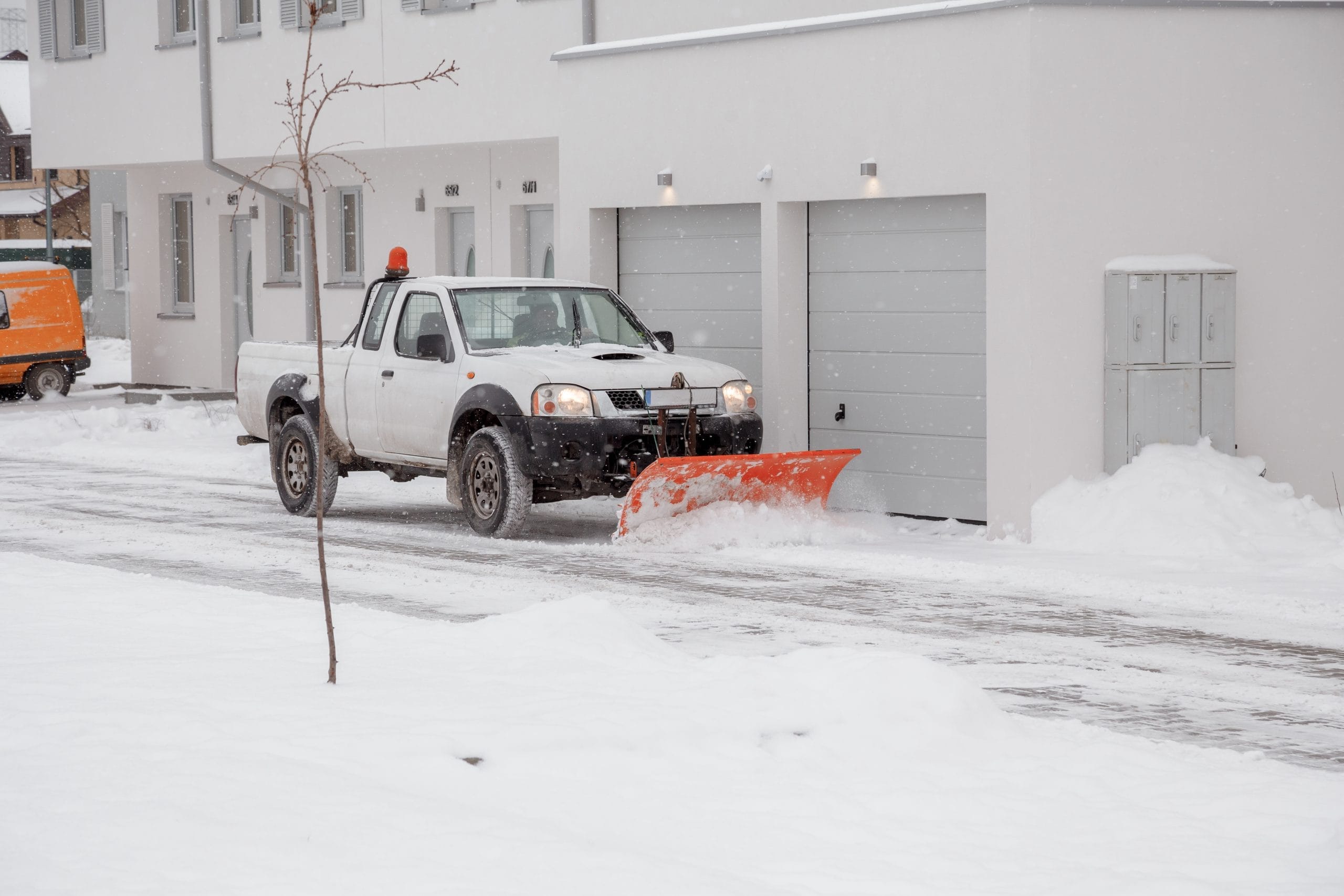 A pickup truck with a snowplow clears snow from a suburban street near houses in winter.